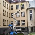 Montaż kolców przeciw ptakom z podnośnika koszowego na budynku szkoły