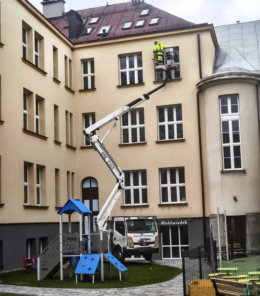 Montaż kolców przeciw ptakom z podnośnika koszowego na budynku szkoły